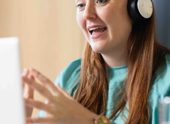 At office, Wearing headphones, woman video on video call on laptop, engaging in remote work. remote working, telecommuting, technology, business, communication, workspace