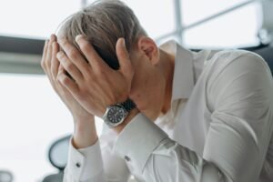 Stressed business professional with head in hands at office desk, indicating workplace frustration or miscommunication.