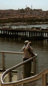 Woman standing by the waterfront railing, overlooking the Golden Horn with a distant palace skyline.