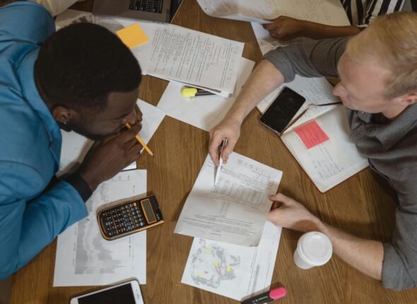 Two professionals working together at a table, reviewing documents, charts, and a calculator, illustrating teamwork and effective communication.