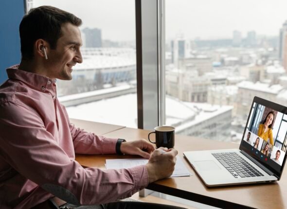 Man in business shirt attending a virtual meeting with colleagues via laptop in a modern office with a city view